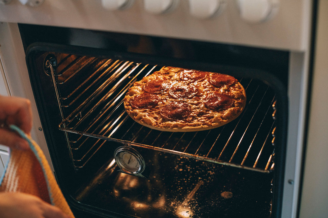Homemade pizza is baked in an oven with a thermometer.