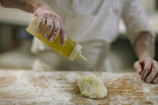 A person adding olive oil to the pizza dough